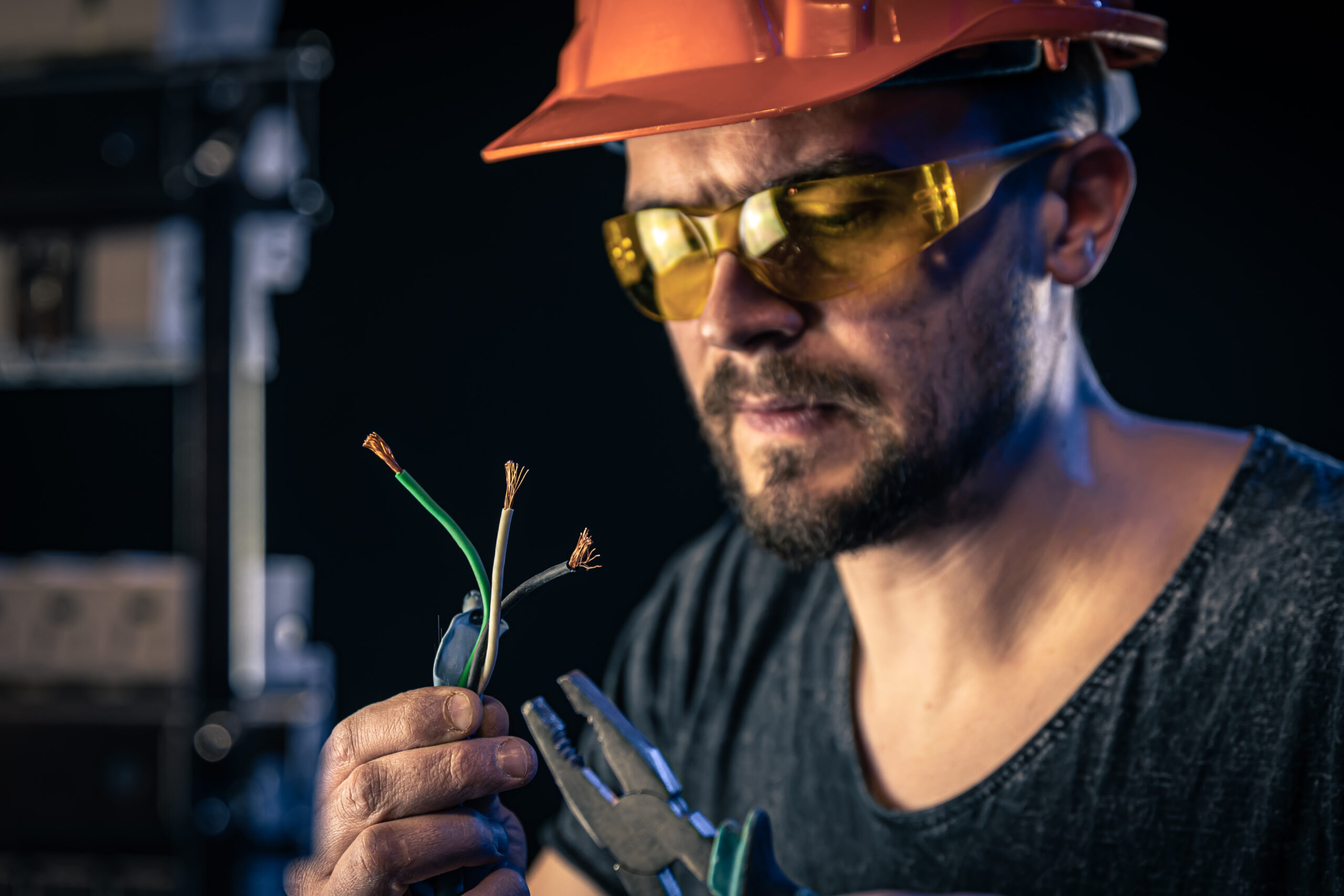 A male electrician in a protective helmet works in a switchboard with an electrical connecting cable.